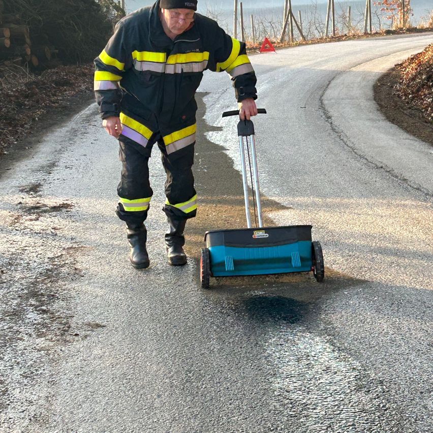 Ein Mann in einem gelben und schwarzen Sicherheitsanzug schiebt eine Maschine auf einer nassen Straße und hinterlässt einen schwarzen Fleck.