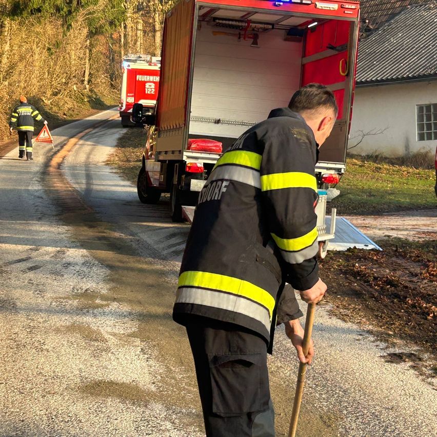 Ein Feuerwehrmann reinigt Straßenschmutz, während ein Feuerwehrwagen in der Nähe geparkt ist.