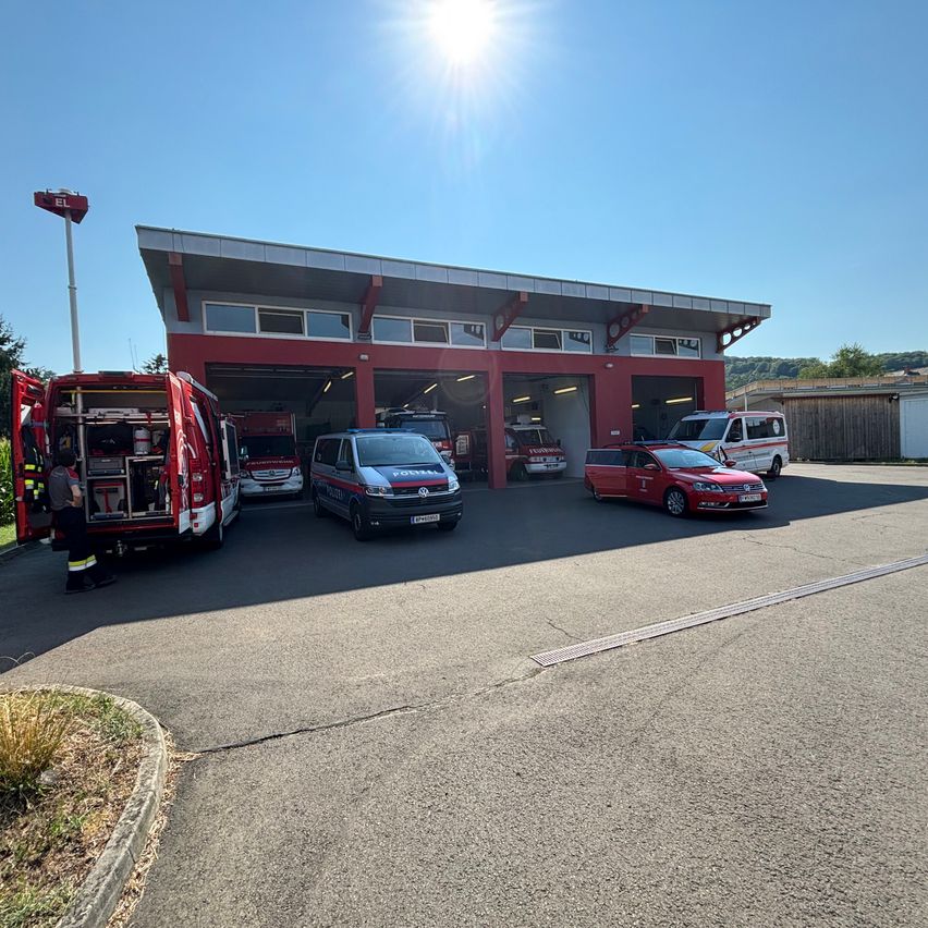 Eine Feuerwehrstation mit mehreren Rettungsfahrzeugen, die unter der hellen Sonne draußen geparkt sind. Eine Person steht in der Nähe eines Feuerwehrwagens.