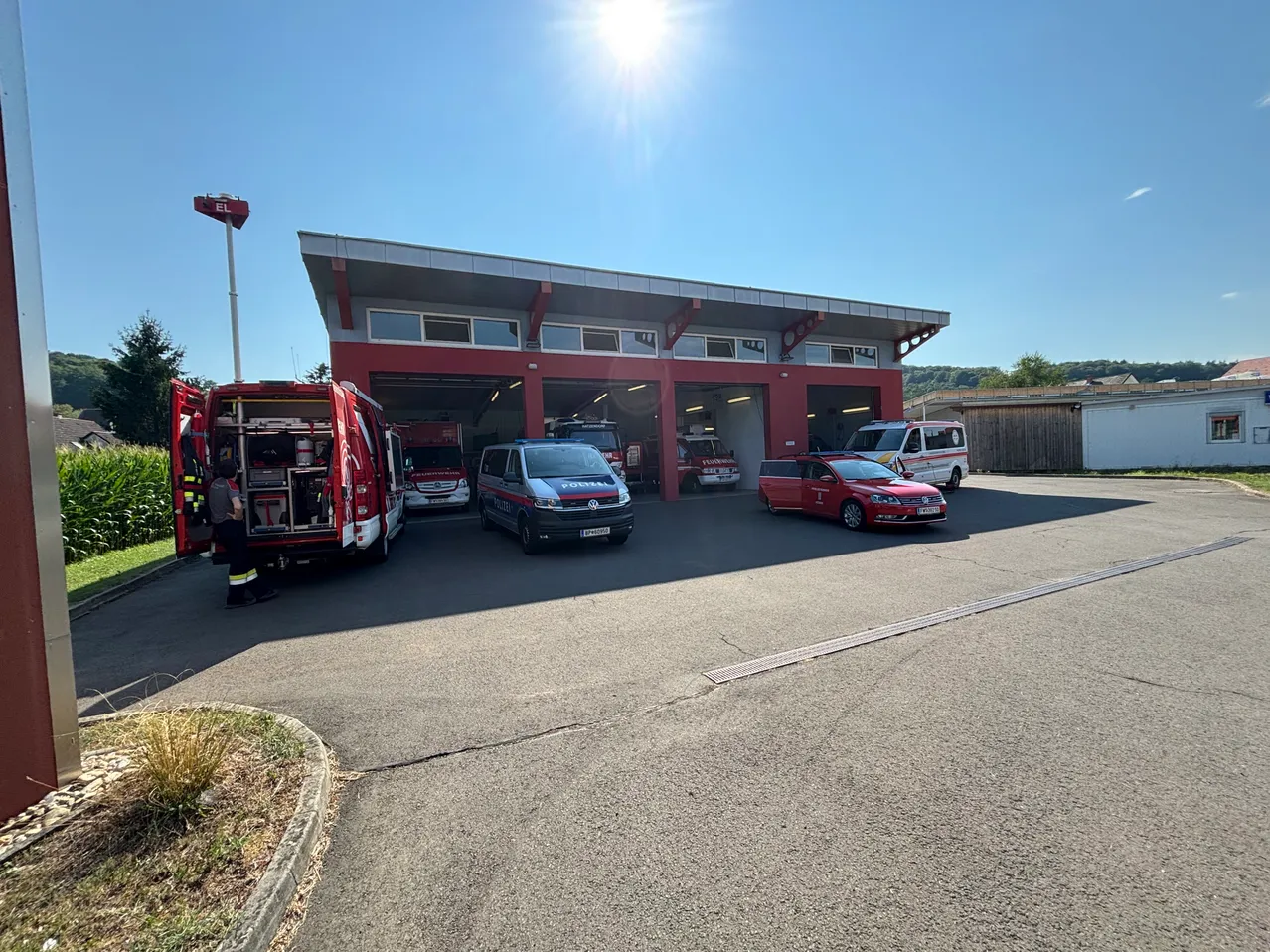 Eine Feuerwehrstation mit mehreren Rettungsfahrzeugen, die unter der hellen Sonne draußen geparkt sind. Eine Person steht in der Nähe eines Feuerwehrwagens.