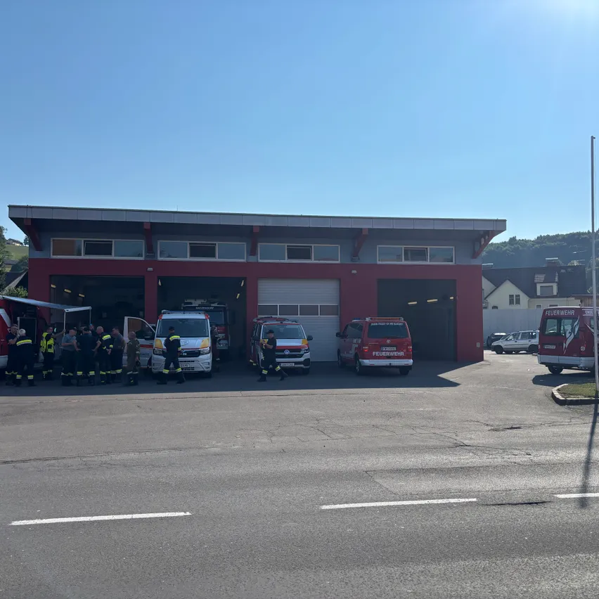 Vor einer Feuerwache sind Rettungsfahrzeuge geparkt, und Feuerwehrleute sind an einem sonnigen Tag in der Nähe versammelt.