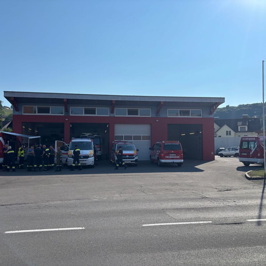 Vor einer Feuerwache sind Rettungsfahrzeuge geparkt, und Feuerwehrleute sind an einem sonnigen Tag in der Nähe versammelt.