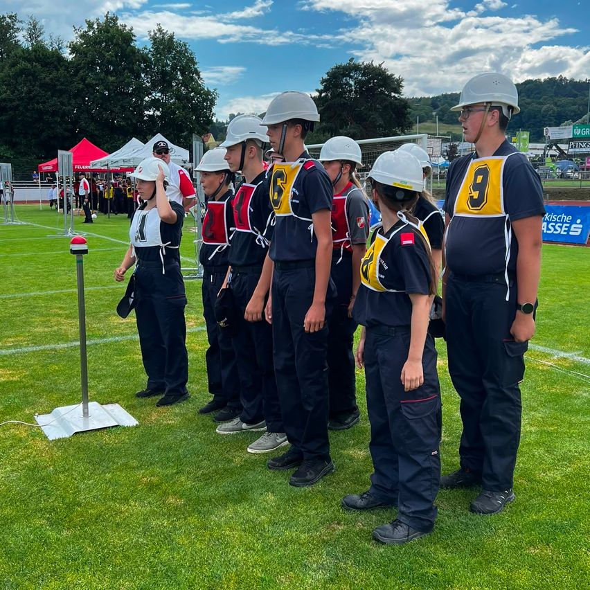Eine Gruppe junger Menschen in Uniformen und Helmen steht auf einem Feld, möglicherweise in Vorbereitung auf eine Sportveranstaltung. Die Nummer 9 ist auf einer der Uniformen deutlich sichtbar.