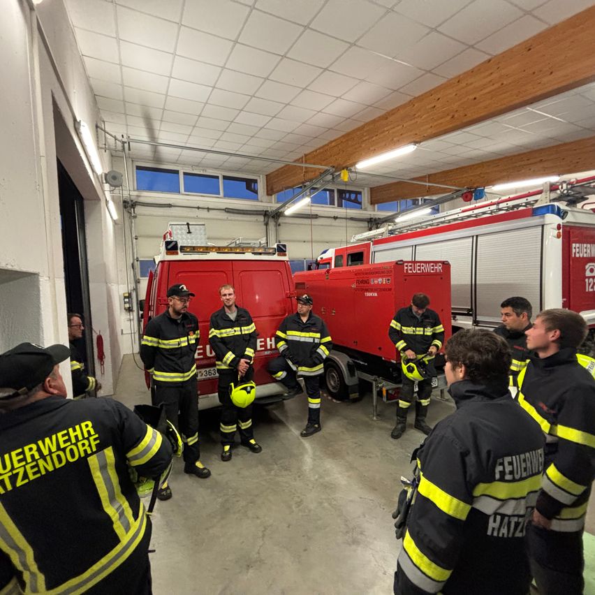 Eine Gruppe von Feuerwehrleuten in Uniform steht in einer Feuerwache, mit Feuerwehrautos im Hintergrund.
