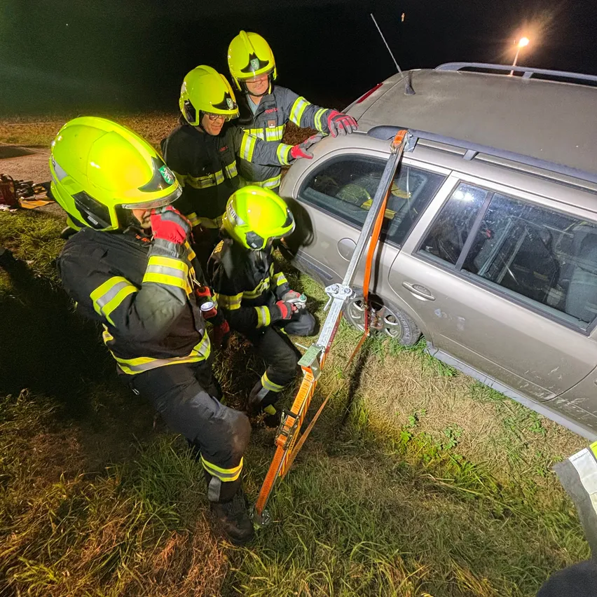 Eine Gruppe von Feuerwehrleuten in gelben Helmen und Uniformen arbeitet an einem umgekippten Auto.