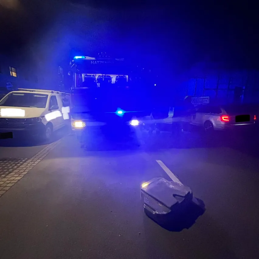 Ein Polizeibus mit blauen Lichtern ist am Straßenrand geparkt. Ein weißer Lieferwagen und ein Auto sind in der Nähe geparkt. Ein Beutel liegt auf der Straße.