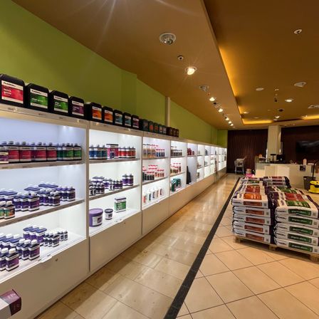 Ein Ladengang mit weißen Regalen, gefüllt mit verschiedenen Flaschen und Behältern von Produkten, und eine Reihe weißer Taschen mit Etiketten auf dem Boden.