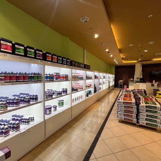 Ein Ladengang mit weißen Regalen, gefüllt mit verschiedenen Flaschen und Behältern von Produkten, und eine Reihe weißer Taschen mit Etiketten auf dem Boden.