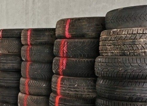 Ein Stapel Reifen mit roten Linien darauf, gestapelt gegen eine graue Betonwand. Die Reifen sehen alt und abgenutzt aus.