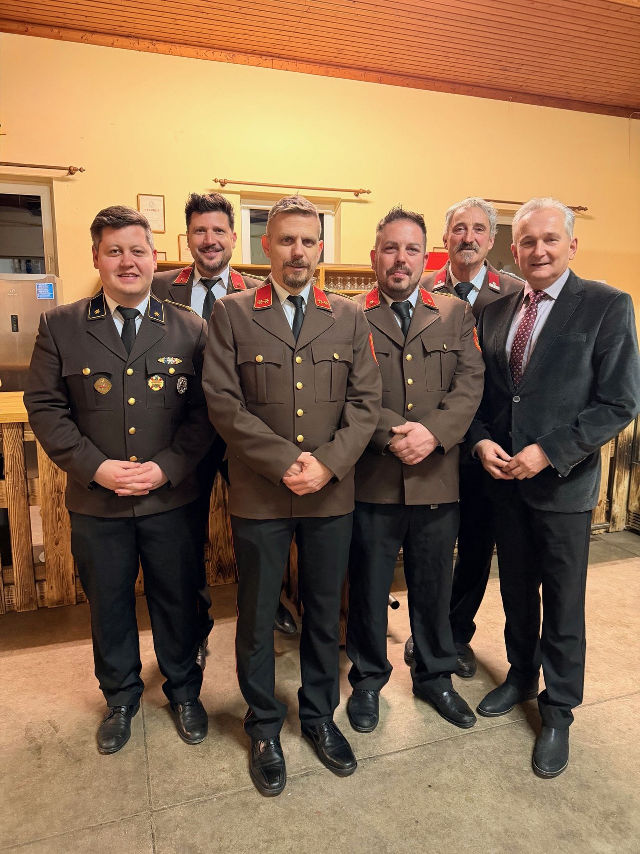 Sechs Männer in formeller Kleidung stehen zusammen, wahrscheinlich bei einer formellen Veranstaltung. Vier tragen Militäruniformen, während zwei in Anzügen an den Seiten stehen. Sie alle lächeln und scheinen für ein Foto zu posieren.