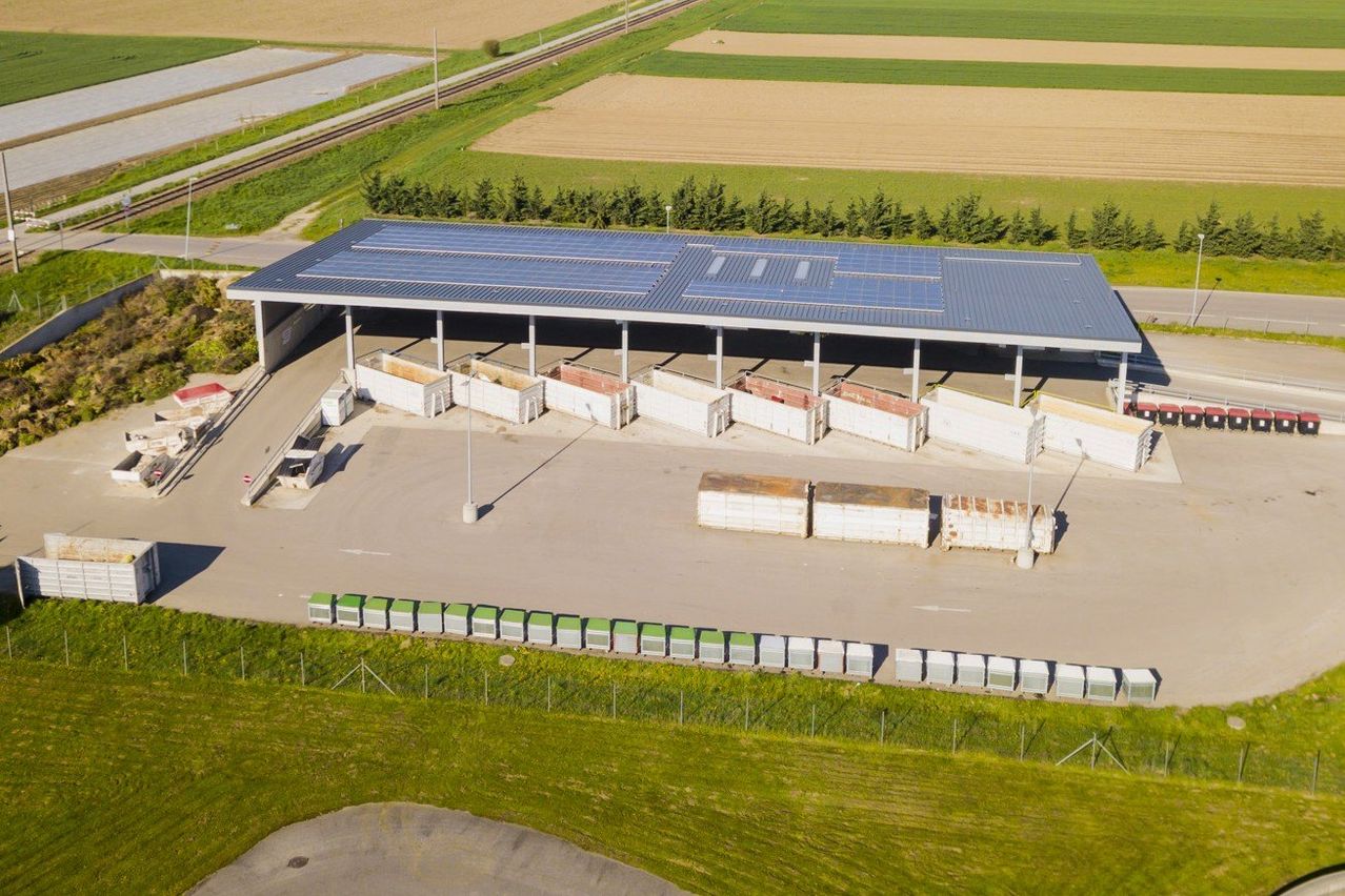 Luftaufnahme einer solarbetriebenen Anlage mit mehreren Lagercontainern und einer großen Solarpanel-Anlage auf dem Dach.