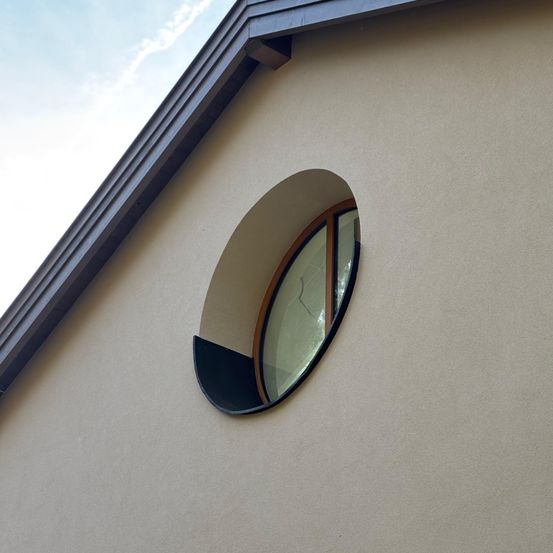Ein Gebäude mit einer beigefarbenen Wand und einem schwarz umrandeten runden Fenster darauf.