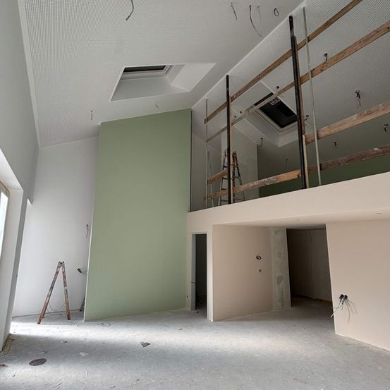 Ein Innenraum eines Raumes im Bau. Die Wände sind weiß und grün gestrichen. Eine Leiter lehnt an der Wand.