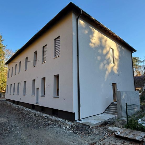Ein neues Wohnhaus mit vielen Fenstern wird gebaut. Es ist ein zweistöckiges Gebäude mit einem Flachdach und einer Treppe, die zum Eingang führt.