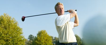 Ein Mann schwingt einen Golfschläger auf einem Golfplatz mit grünem Gras und Bäumen im Hintergrund.
