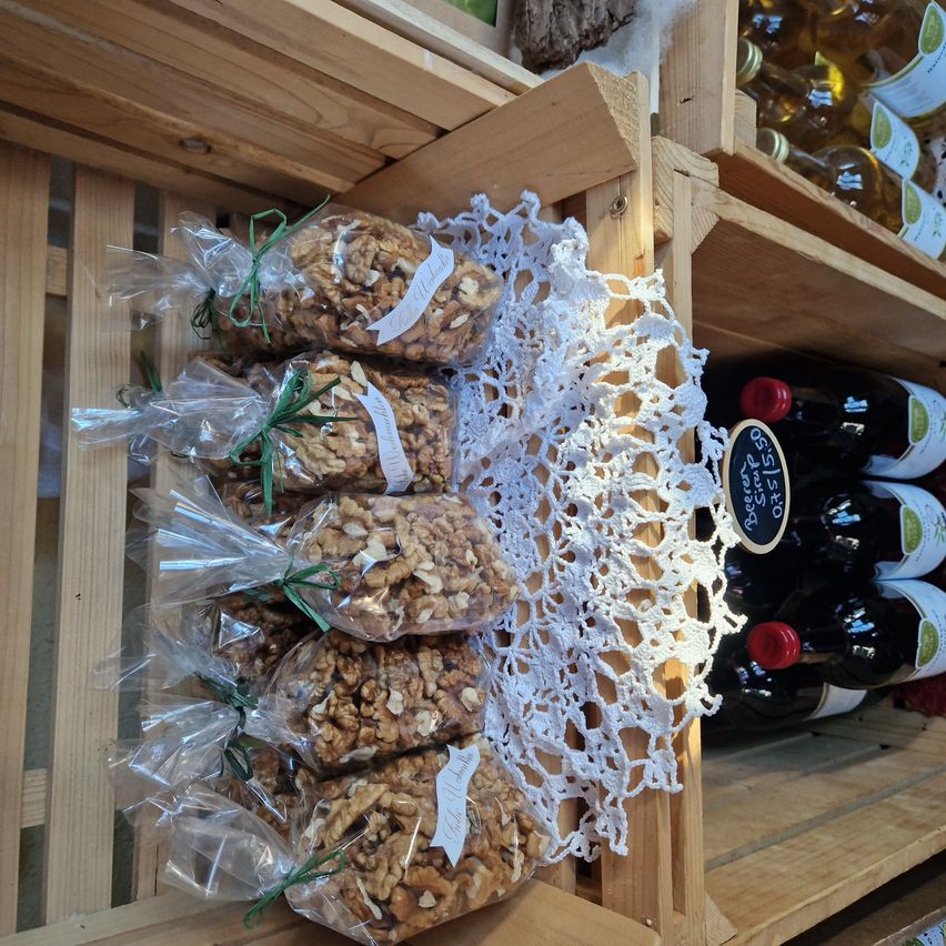 Eine Holzkiste gefüllt mit Tüten von Walnüssen, in Plastik verpackt und mit einer weißen Spitze verziert. Dahinter zeigt ein Holzregal mehrere Flaschen Wein.