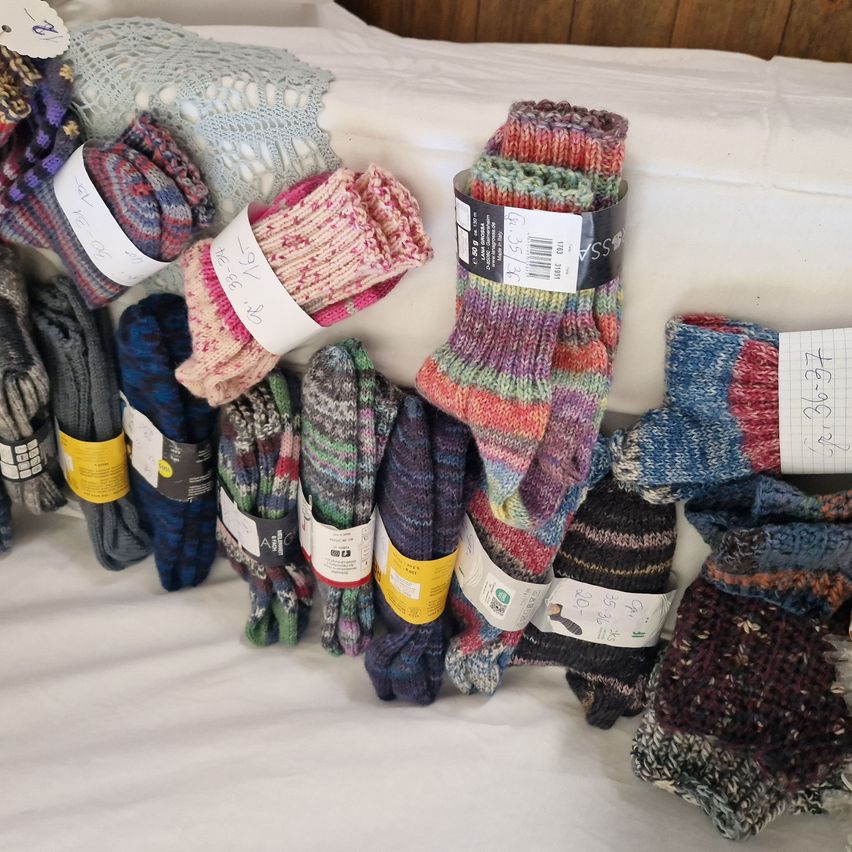 Various colorful hand-knitted socks with price tags and notes are displayed on a white surface.