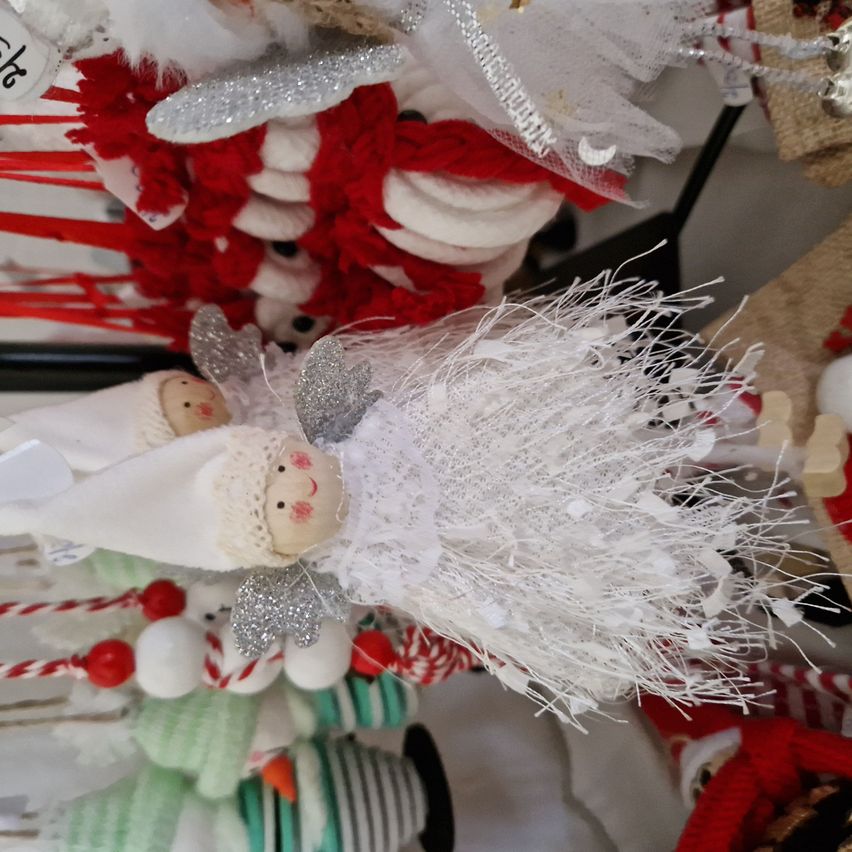 Eine Sammlung von Weihnachtsdekorationen zeigt einen weißen Engel mit einem weißen Kleid und silbernen Flügeln, umgeben von roten und weißen Objekten und anderen Dekorationen.