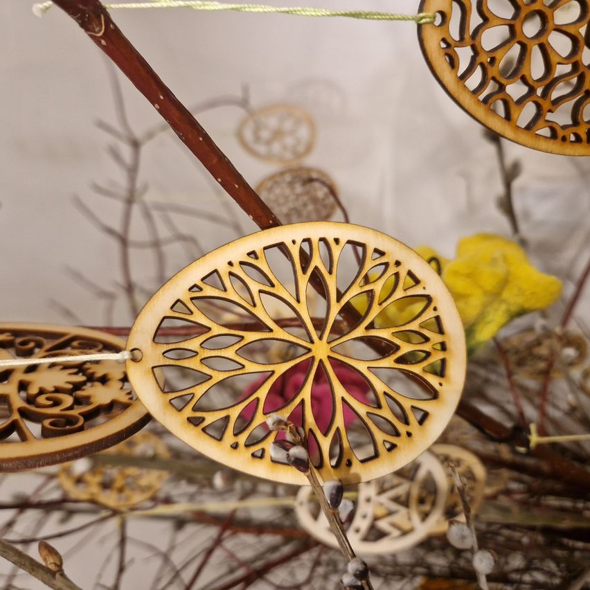 Holzverzierungen hängen von Ästen mit komplizierten Designs, umgeben von gelben und roten Blumen. Die Verzierungen haben unterschiedliche Größen und Formen.