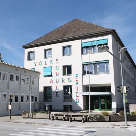 Ein weißes Gebäude mit dem Namen 'Volkshochschule Friedberg', das an einer Straße steht.