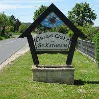 Ein Schild für Gruss Golf in St.Kathrein steht am Straßenrand, umgeben von Grün und einem Zaun.