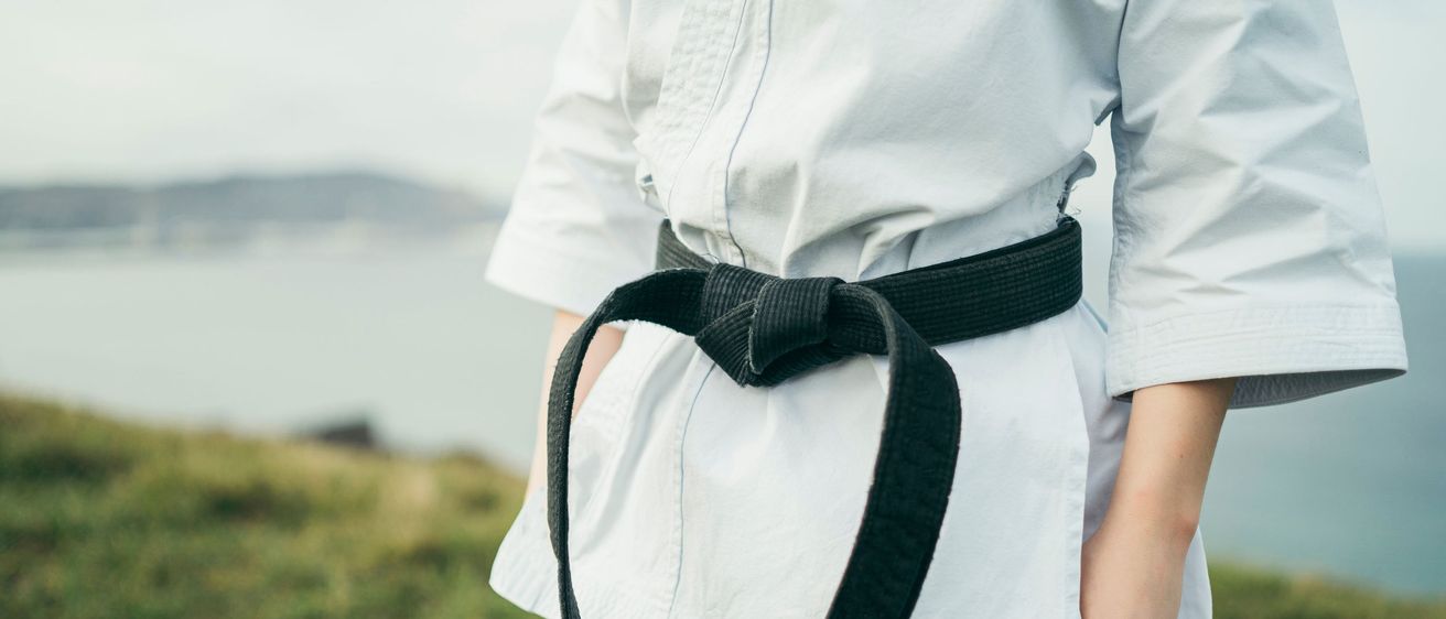 Eine Person, die in einem weißen Karate-Anzug gekleidet ist, steht auf einem Grasfeld und hält den Gürtel um die Taille.