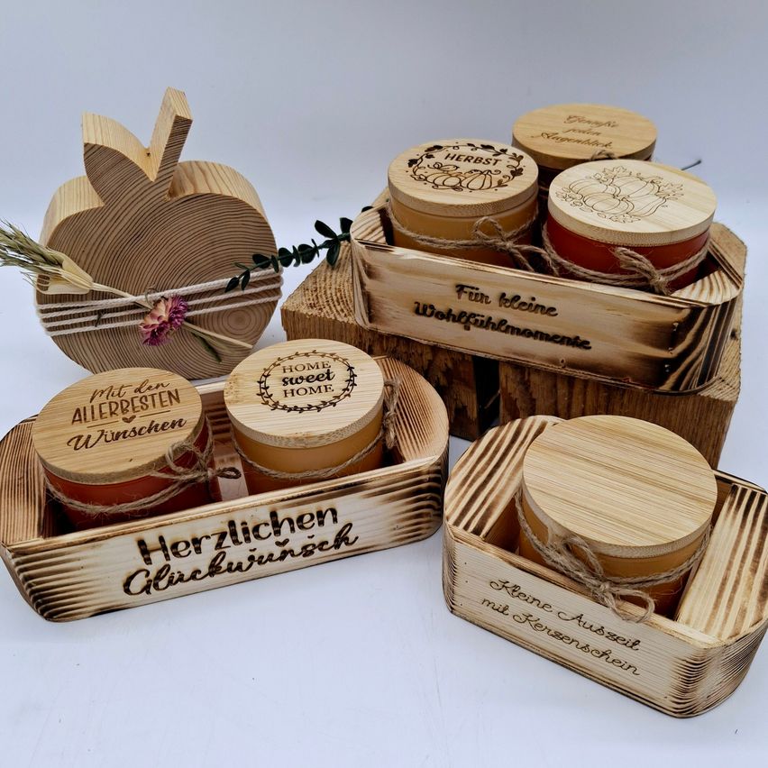 Eine Sammlung von Holzkisten und Gläsern mit personalisierten Etiketten, darunter 'Home Sweet Home' und 'Herbst', auf einer weißen Oberfläche angeordnet.