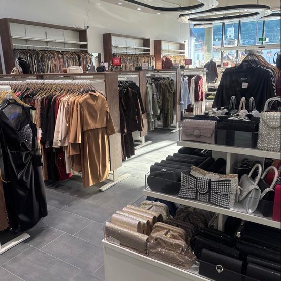 Ein Innenbekleidungsgeschäft mit verschiedenen Kleiderständern und Handtaschen zur Schau. Der Laden hat ein modernes und organisiertes Layout mit einer Vielzahl von Kleidungsstücken und Accessoires.