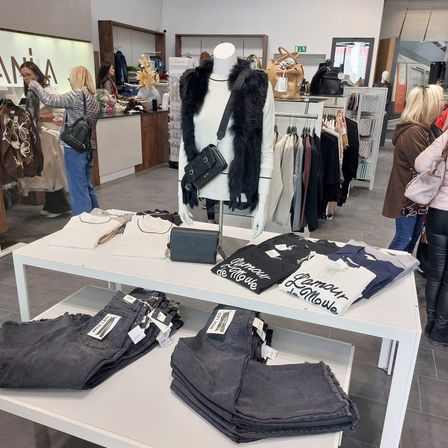 Ein Bekleidungsgeschäft mit einer Puppe, die einen Pelzmantel und eine schwarze Tasche trägt, einem Tisch mit gefalteten Jeans und T-Shirts und Kunden, die stöbern.
