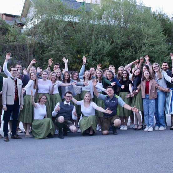 Eine Gruppe von Menschen in traditioneller Kleidung, die lächelnd und posierend für ein Gruppenfoto vor Bäumen stehen.