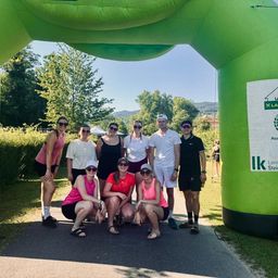 Eine Gruppe von Menschen posiert für ein Foto vor einem grünen aufblasbaren Tor, mit einem Berg im Hintergrund.