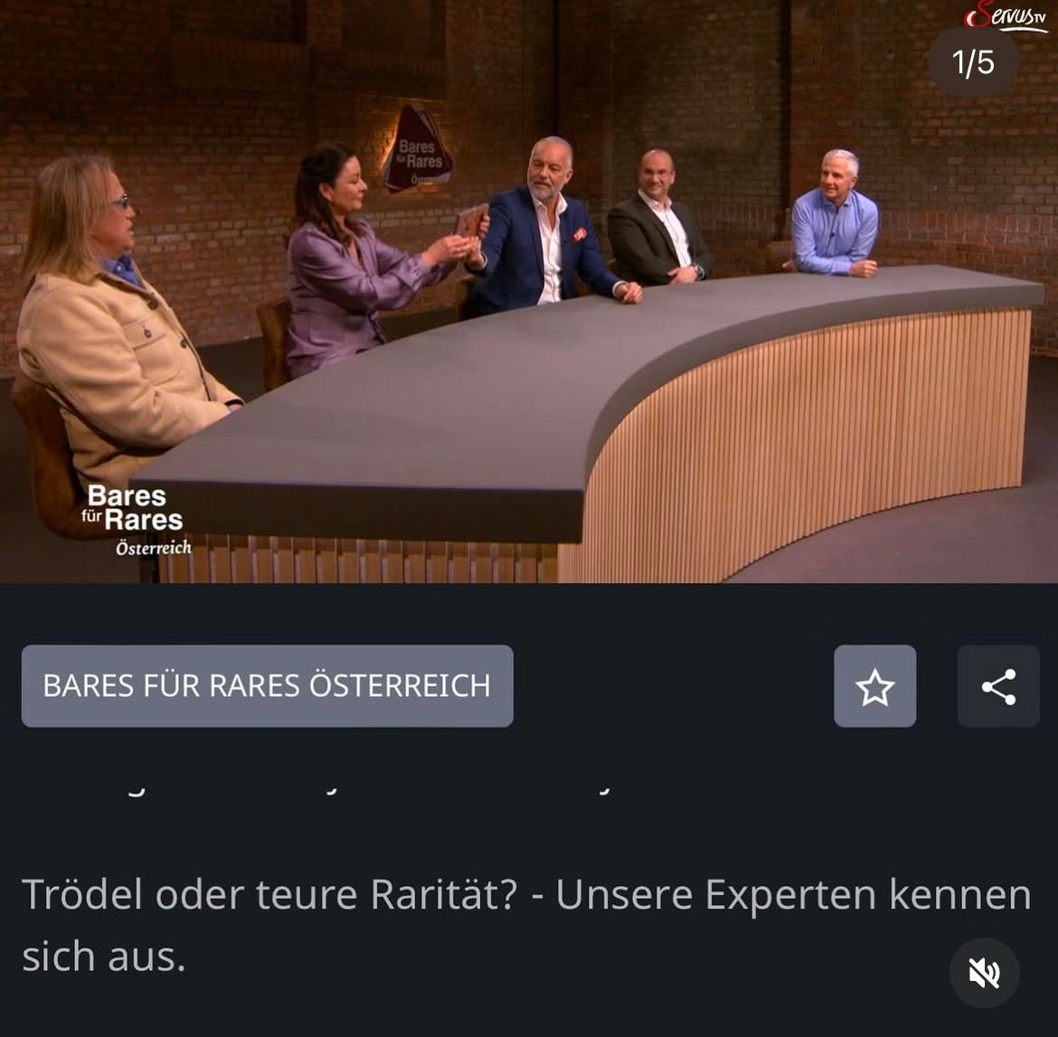 Fünf Personen sitzen um einen Tisch herum. Drei Männer und zwei Frauen. Sie sind wahrscheinlich in einer Talkshow. Der Text lautet 'Bares für Rares Österreich'. Der untere Text lautet 'Trödel oder teure Rarität?'.