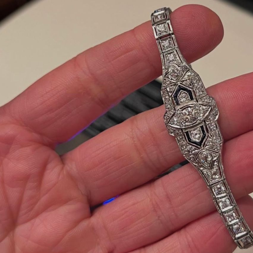 Eine Hand hält eine Vintage-Armbanduhr mit Blumenmotiv und schwarzem Email, verziert mit zahlreichen Diamanten.