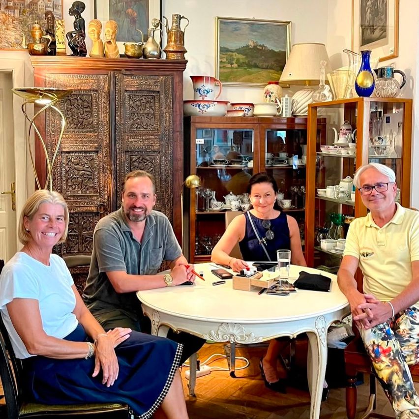 Four people are sitting around a table in a room with decorative items and a cabinet.