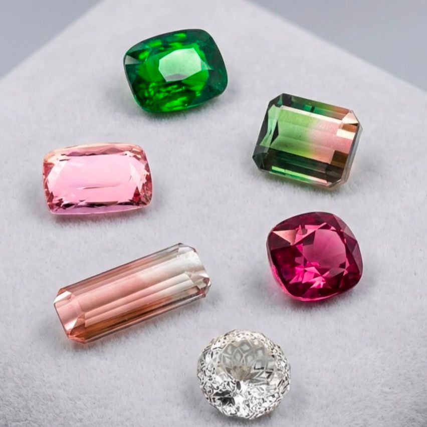 A collection of gemstones, including emeralds, tourmalines, and rubies, arranged on a white cloth.