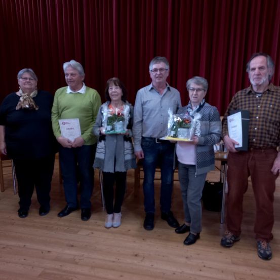 Eine Gruppe von Menschen posiert für ein Foto mit Blumen und Urkunden in der Hand vor einem roten Vorhang.