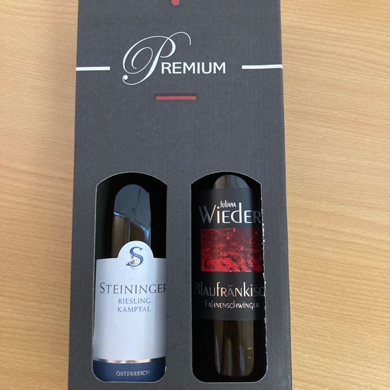 Eine schwarze Premium-Box zeigt zwei Weinflaschen. Die linke Flasche ist Steininger Riesling Kamptal aus Österreich. Die rechte Flasche ist Juliana Wieder Blaufränkisch mit rotem Etikett.