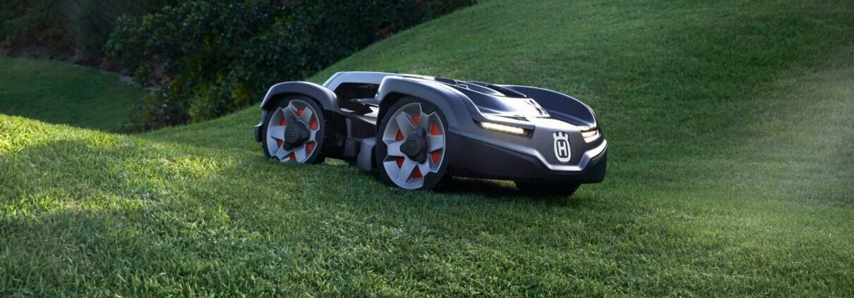 Ein schlanker, schwarzer robotergesteuerter Rasenmäher mit silberner Felge und roten Akzenten an den Rädern steht auf einem grünen Rasen.