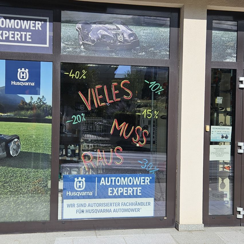 Ein Schaufenster zeigt einen Rasenmäher mit verschiedenen Rabatten in Rot auf der Scheibe. Das Schild sagt 'AUTOMOWER EXPERTE' und beinhaltet ein Husqvarna-Logo.