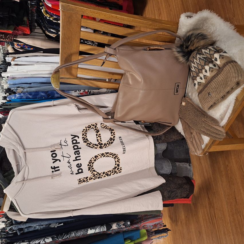 Ein Stapel Kleidung und Accessoires auf einem Holzstuhl. Beinhaltet eine beige Handtasche, Leoparden-Print-Kapuzenjacke, Strickmütze und Handschuhe.