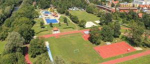 Luftaufnahme eines Sportkomplexes mit Schwimmbad, Fußballfeld, Laufbahn und Tennisplätzen.