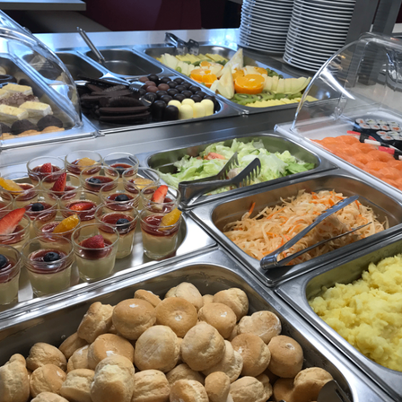 Ein Buffettisch mit verschiedenen Desserts und herzhaften Gerichten. Zu den Desserts gehören Schokoladen, Fruchtbecher und Gebäck. Zu den herzhaften Optionen gehören Salate, Sushi und Kartoffelpüree.