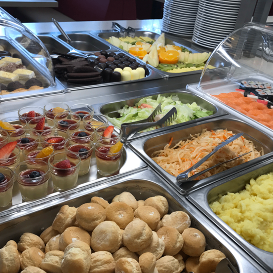 Ein Buffettisch mit verschiedenen Desserts und herzhaften Gerichten. Zu den Desserts gehören Schokoladen, Fruchtbecher und Gebäck. Zu den herzhaften Optionen gehören Salate, Sushi und Kartoffelpüree.