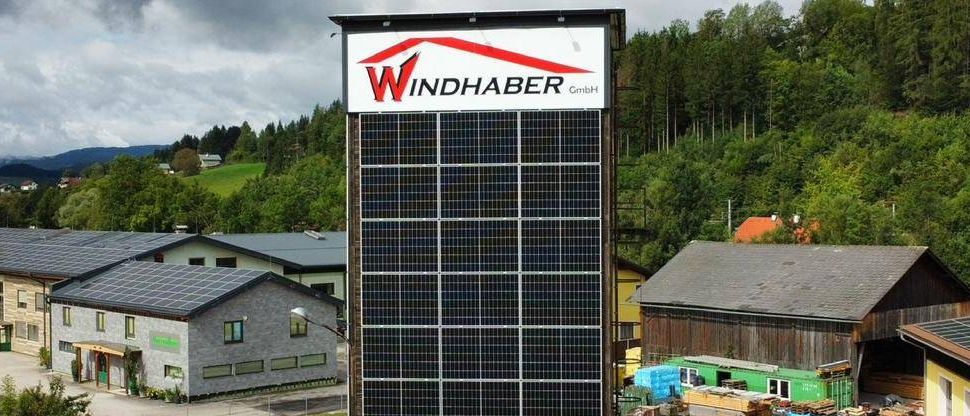 Eine Draufsicht auf ein Gebäude mit einem großen Solarpanel an der Seite. Es ist von anderen Gebäuden, einer Straße und einem Wald umgeben.