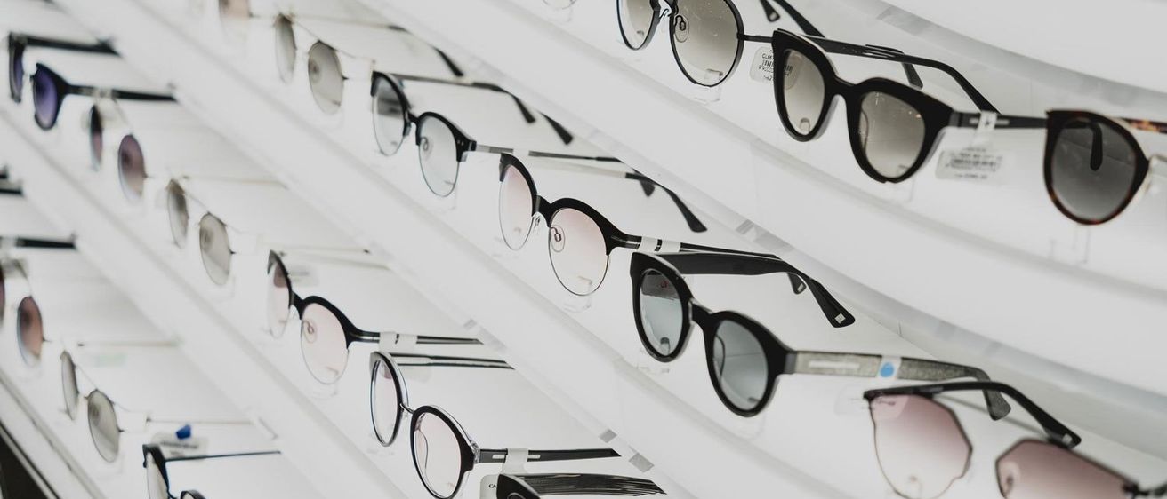 Eine Sammlung von Sonnenbrillen in verschiedenen Farben und Stilen, ordentlich auf einem weißen Regal angeordnet und ihre Gläser und Rahmen präsentierend.