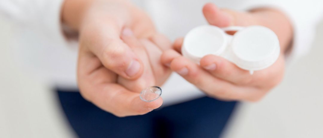 Eine Person hält eine Kontaktlinse in den Händen und bereitet sich darauf vor, sie in ein Auge einzusetzen. Die Linse ist klar und ruht auf einem Finger.