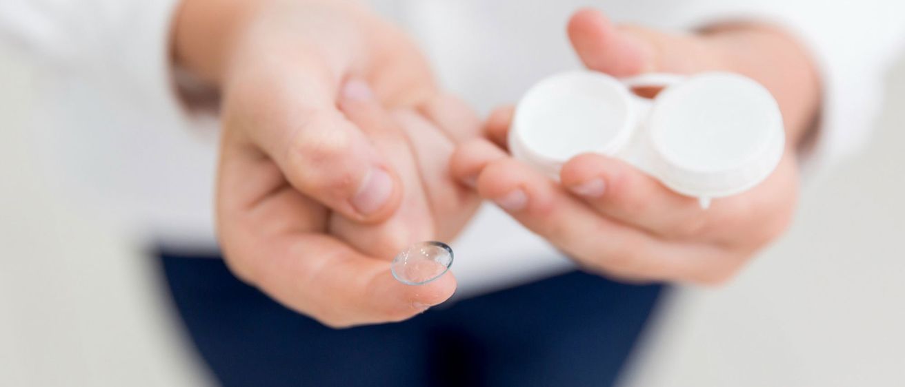 Eine Person hält eine Kontaktlinse in den Händen und bereitet sich darauf vor, sie in ein Auge einzusetzen. Die Linse ist klar und ruht auf einem Finger.