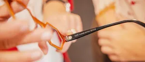 Ein Paar Brille mit orangefarbenen Gläsern wird von einer Person gehalten. Die Brille hat den Text 'Waldviertler Brille' auf der Seite.