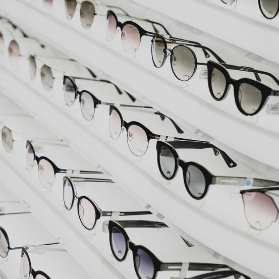 Mehrere Sonnenbrillenpaare sind auf weißen Regalen ausgestellt und zeigen verschiedene Stile und Rahmen.