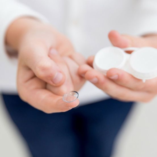 Eine Hand hält eine Kontaktlinse in einer Hand und eine Kontaktlinsenbox in der anderen.